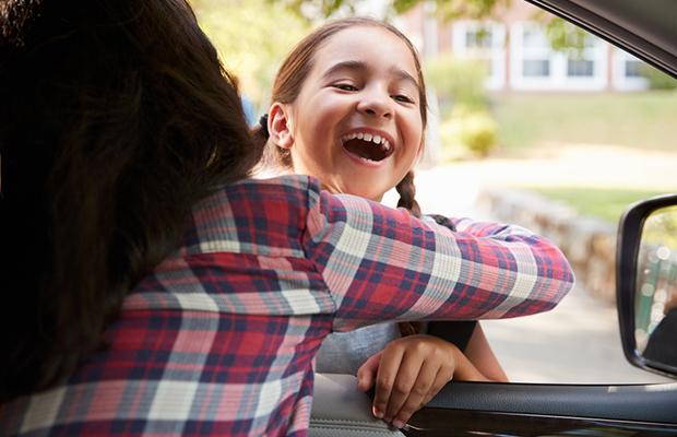 lady hugging young, smiling girl through car window